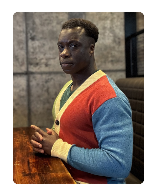 Person wearing a colorful sweater sitting at a table with a textured wall background